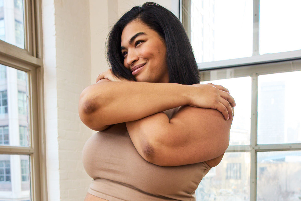 Model in a beige tank top hugging herself